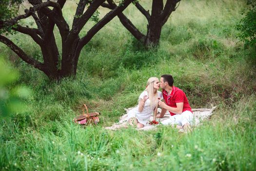 couple in love a blonde girl and a guy in a red t-shirt at a picnic in a park with green grass