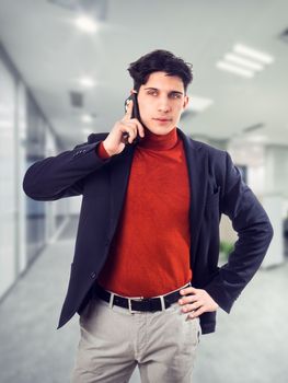 Handsome young businessman in his office talking on cell phone, looking to a side, serious