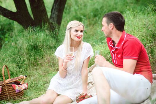 couple in love a blonde girl and a guy in a red t-shirt at a picnic in a park with green grass