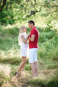 couple in love a blonde girl and a guy in a red t-shirt at a picnic in a park with green grass