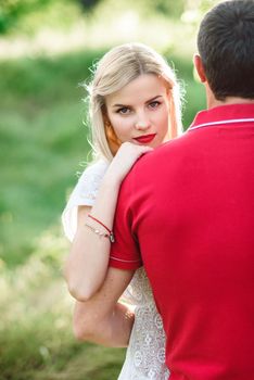 couple in love a blonde girl and a guy in a red t-shirt at a picnic in a park with green grass