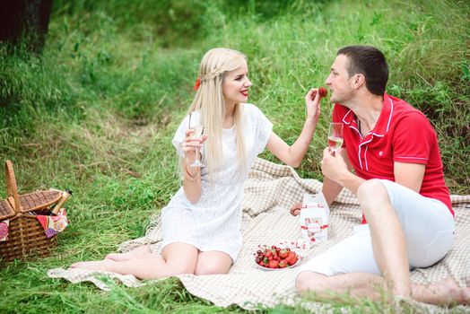 couple in love a blonde girl and a guy in a red t-shirt at a picnic in a park with green grass