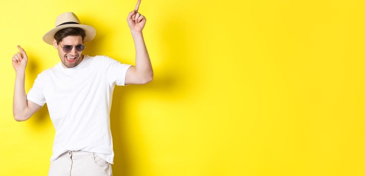 Tourism, travelling and holidays concept. Male tourist enjoying vacation, dancing in straw hat and sunglasses, pointing fingers sideways.