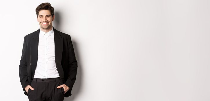 Image of handsome caucasian man in party suit, smiling pleased, attend formal event, standing over white background.