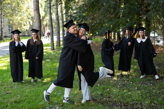 A group of graduates in robes congratulate each other on their graduation outdoors