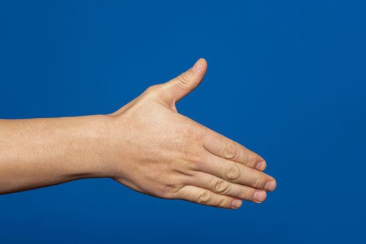 Man stretching out his hand to handshake isolated on a blue background. Man's hand ready for handshake