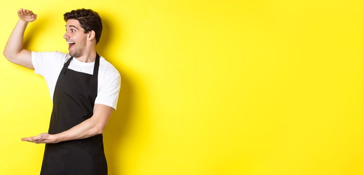 Man looking surprised at something large, standing in black apron against yellow background.