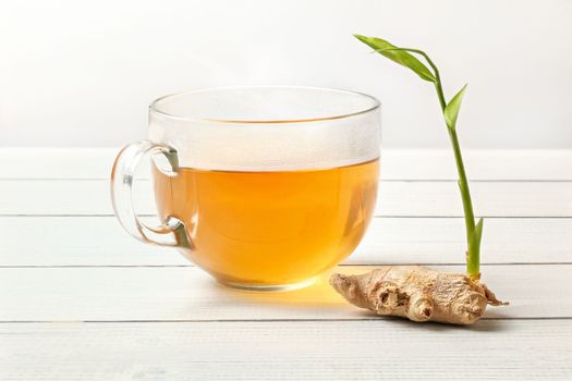 Dry ginger root with green sprout on white boars table, glass cup of freshly brewed tea next to it.