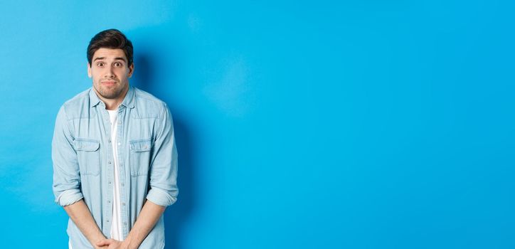 Embarrassed guy want to pee, waiting in line for toilet, standing against blue background.