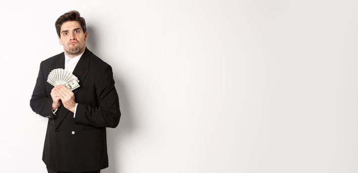 Image of greedy guy in black suit, holding money and unwilling to share, standing over white background.