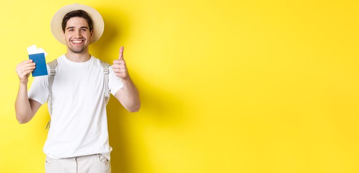 Tourism and vacation. Satisfied male tourist showing passport with tickets and thumb up, recommending travel company, standing over yellow background.