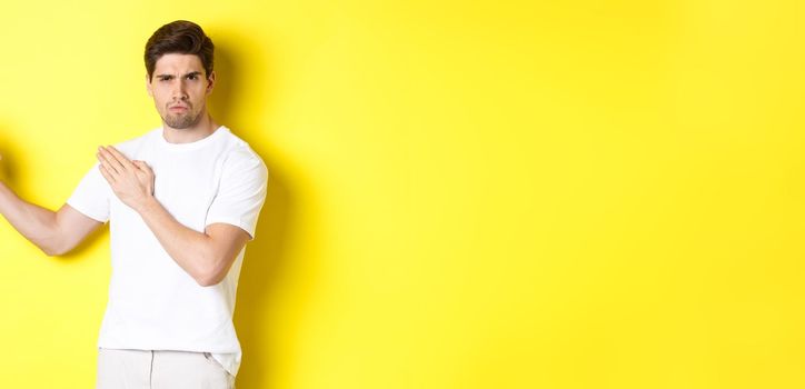 Man showing kung-fu skills, martial arts ninja movement, standing in white t-shirt ready to fight, standing over yellow background. Copy space