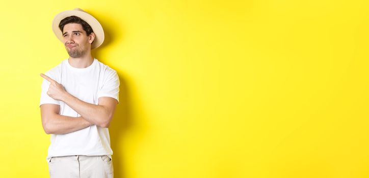 Concept of tourism and lifestyle. Displeased male tourist complaining, looking and pointing finger at upper left corner promo with disappointment, standing against yellow background.