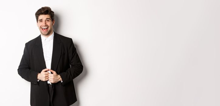 Concept of new year party, celebration and lifestyle. Portrait of handsome and confident man in suit, smiling pleased, feeling successful, standing over white background.