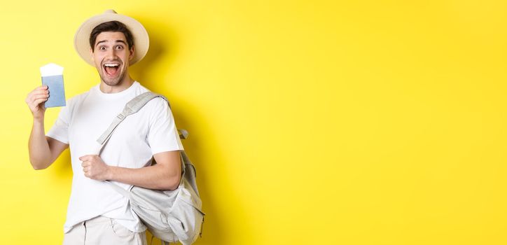 Tourism and vacation. Excited guy tourist going on holiday trip, showing passport with tickets and holding backpack, standing over yellow background.