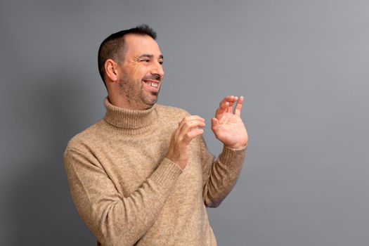 Bearded hispanic man wearing a turtleneck pulled to the side with his hands in front in a gesture of embarrassment and shyness, isolated over gray background