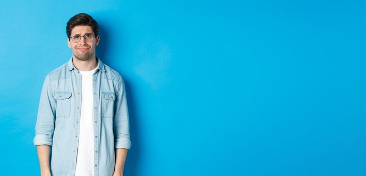 Skeptical and doubtful guy in glasses, looking confused at something strange, blue background.