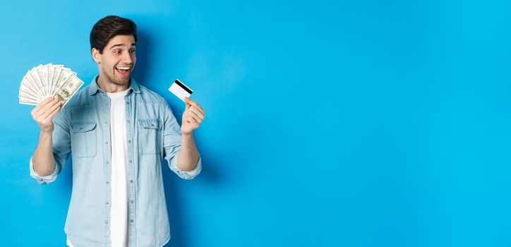 Surprised and happy man looking at credit card and showing money, concept of bank loan, finance and income. Copy space