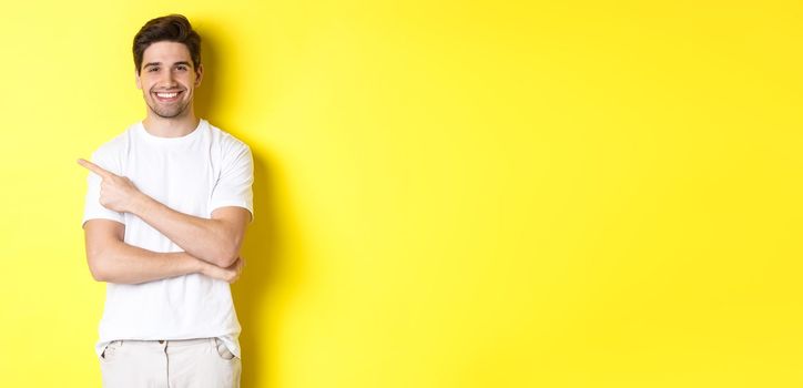 Handsome guy pointing left and smiling, showing advertisement on yellow copy space.