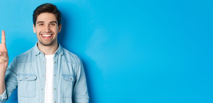 Close-up of handsome man smiling, showing fingers number three, standing over blue background.