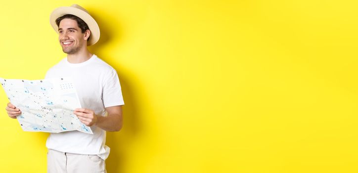 Travelling, vacation and tourism concept. Handsome guy tourist going sightseeing, holding map and smiling, standing over yellow background.