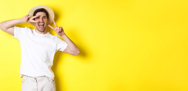 Concept of tourism and vacation. Happy man tourist posing for photo with peace signs, smiling excited, standing against yellow background.