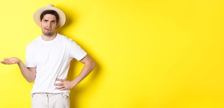 Concept of tourism and summer. Young skeptical tourist complaining, looking judgemental, standing over yellow background.