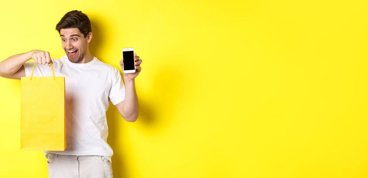 Happy man looking at shopping bag and showing mobile phone screen. Concept of online banking and money.