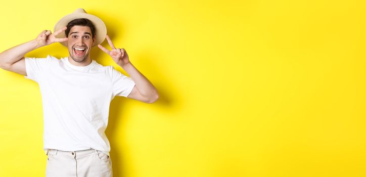 Concept of tourism and vacation. Happy man tourist posing for photo with peace signs, smiling excited, standing against yellow background.