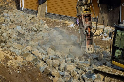 An excavator with jackhammer hydraulic hammer working on smashing lot of stones for road building
