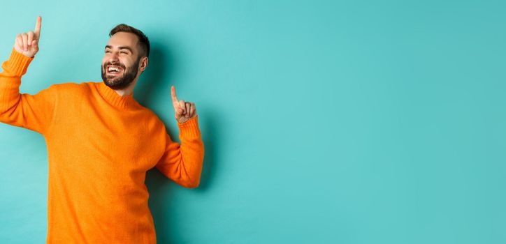 Handsome man celebrating, feeling winner, pointing fingers up and do champion dance, standing over light blue background.