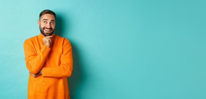 Thoughtful bearded guy making choice, shopping and looking at upper left corner, smiling satisfied, standing over turquoise background.