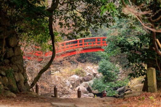 Red bridge crosses rocky creek in forested Japanese landscape. High quality photo