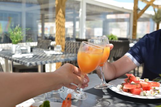 Hands of man and women with glasses of juice in the hands in a restaurant on holidays.