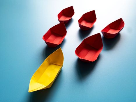 Leadership Concept - Yellow color paper ship origami leading the rest of the red paper ship on blue cover background. Copy space