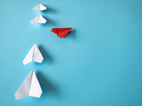 Red paper plane origami leaving other white planes on blue background. Leadership skills concept.