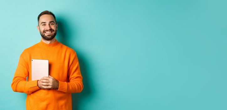 Handsome freelancer man holding laptop and smiling, standing happy over light blue background.