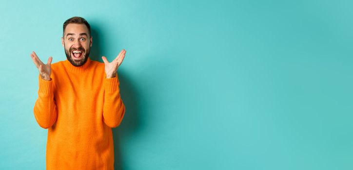 Image of excited and happy bearded man, shaking hands and smiling amazed, telling big news, standing over light blue background.