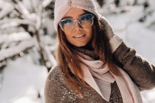 A girl in a sweater and glasses in winter in a snow-covered forest.