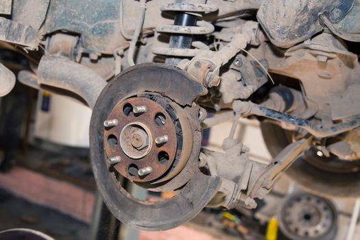 The rear wheel hub is rusty on an old car. In the garage, a man changes parts on a vehicle. Small business concept, car repair and maintenance service. UHD 4K.