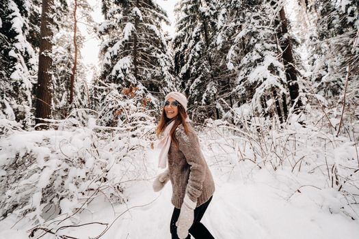 A girl in a sweater and glasses walks in the snow-covered forest in winter.