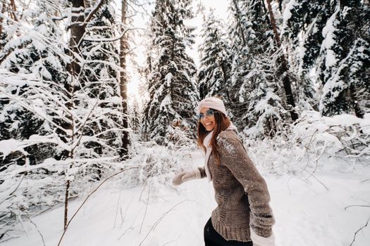 A girl in a sweater and glasses walks in the snow-covered forest in winter.