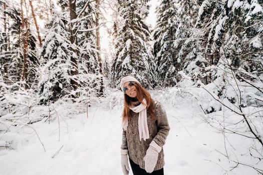 A girl in a sweater and glasses walks in the snow-covered forest in winter.