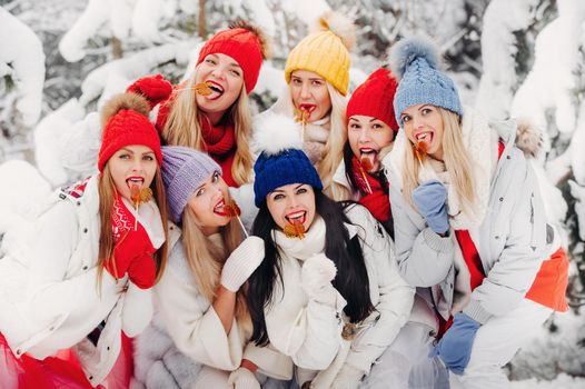 A large group of girls with lollipops in their hands stands in the winter forest.Girls in red and white clothes with candy in a snow-covered forest