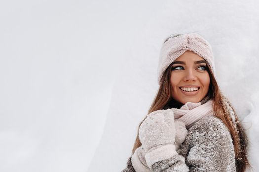 A girl in a sweater and mittens in winter stands on a snow-covered background.