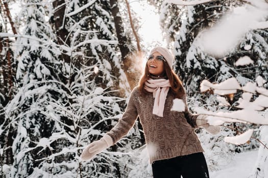 A girl in a sweater and glasses in winter in a snow-covered forest.