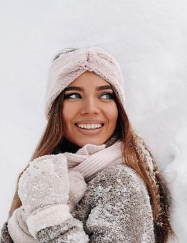 A girl in a sweater and mittens in winter stands on a snow-covered background.