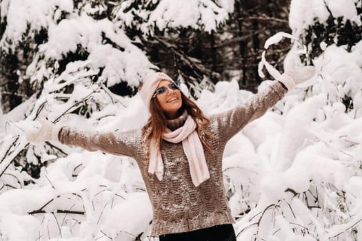 A girl in a sweater and glasses in winter in a snow-covered forest.