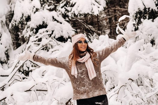 A girl in a sweater and glasses in winter in a snow-covered forest.