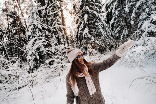 A girl in a sweater and glasses in winter in a snow-covered forest.